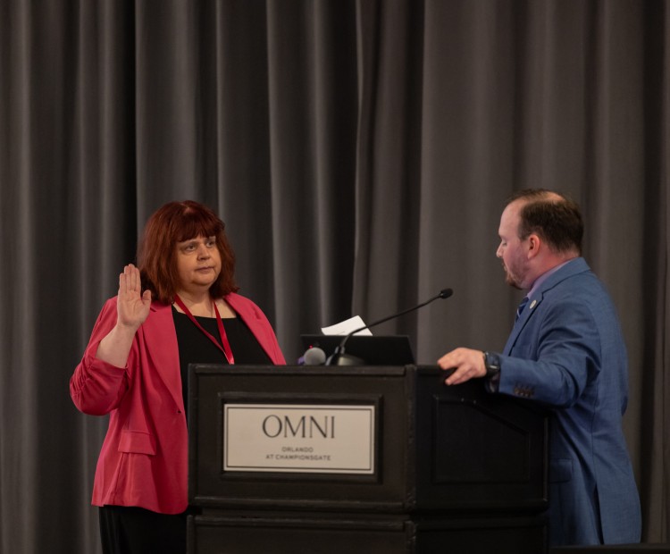 Jutta Bangs with hand up being sworn in as APEX President-Elect
